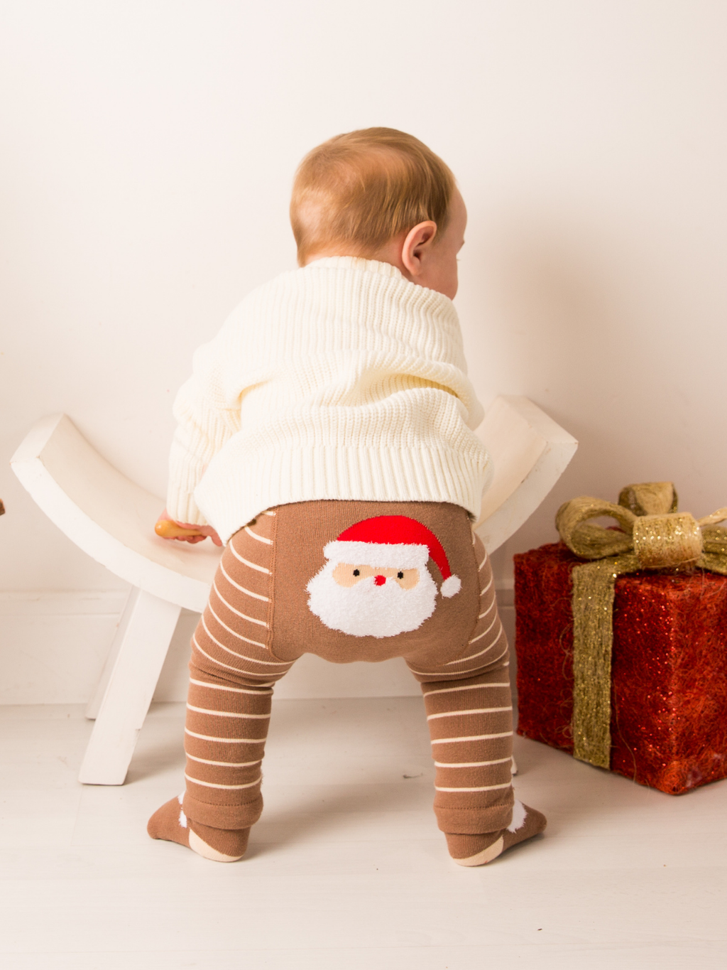 Baby in the cream Believe knitted jumper and Santa striped leggings, back view