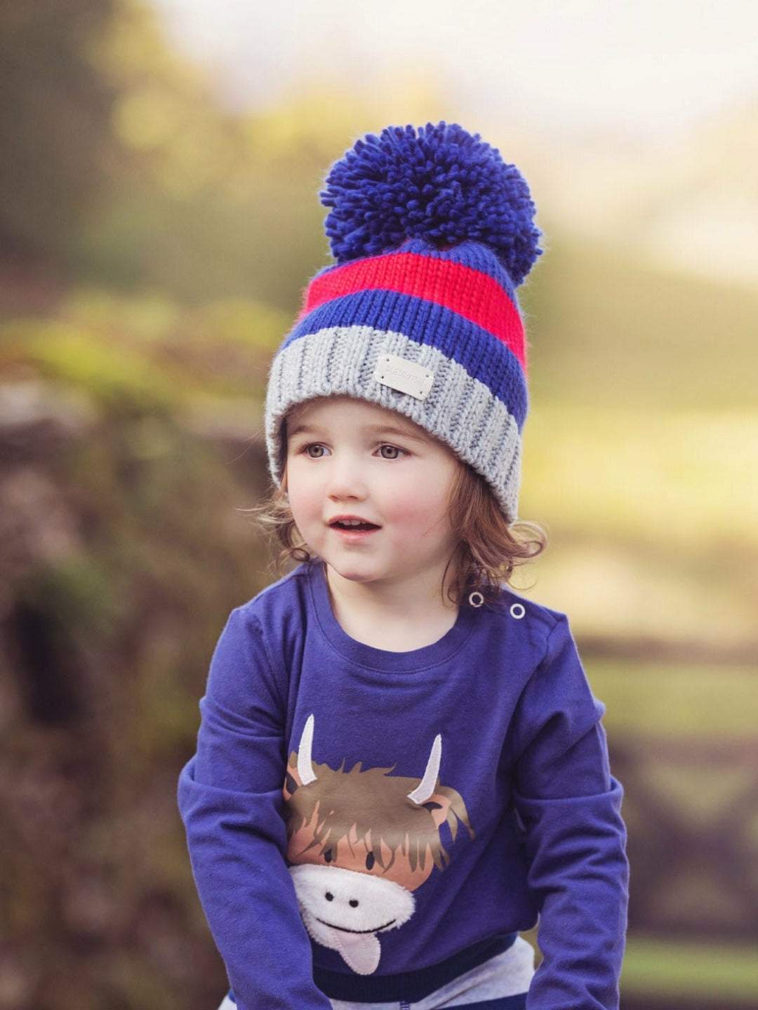 Child Wearing Red and Blue Striped Bobble Hat with Highland Cow Top